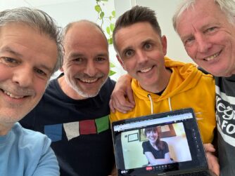 De nieuwe hosts van Looppraat. 4 mannen kijken blij in de camera, Wouter houdt een laptop vast. op het is Anne te zien.