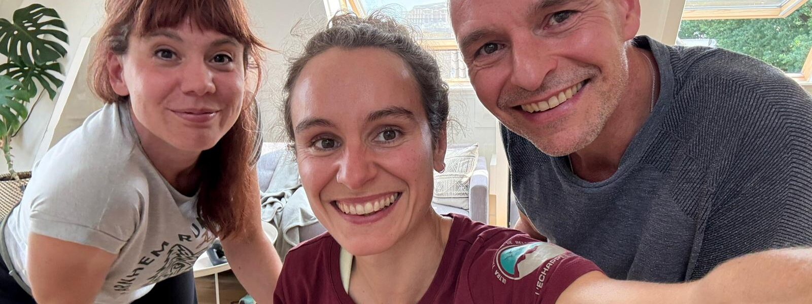Twee jonge vrouwen en een wat oudere man kijken lachend in de camera.
