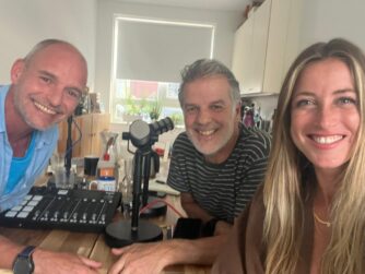 Twee oudere mannen en een jonge vrouw kijken lachend in de camera