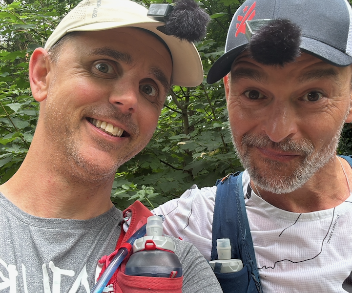 Wouter en Jose met hun armen om elkaar kijken blij de camera in. Ze dragen een pet en hebben allebei een microfoontje aan hun klep geklemd.