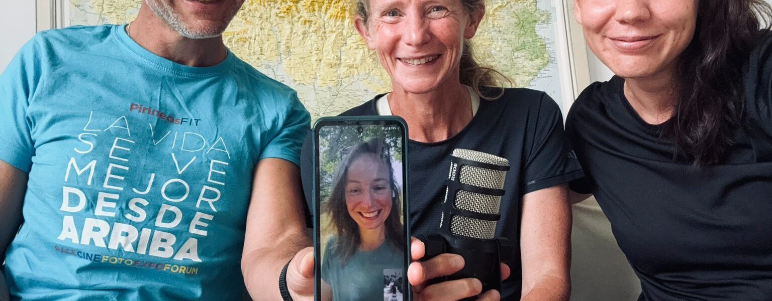 Jose kijkt lachend in de camera en houdt een telefoon beet waarop Noor te zien is. Naast Jose zit Irene in een korte hardloopshort en daarnaast zit Anne