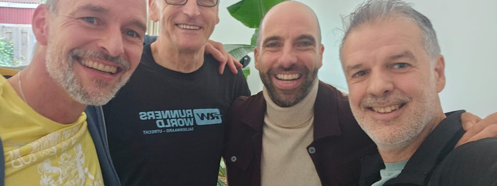 Van ljnks naar rechts kijken Jose, Aart, Bas en Ramiro in de camera. Ze lachen en staan met hun armen over elkaars schouders.